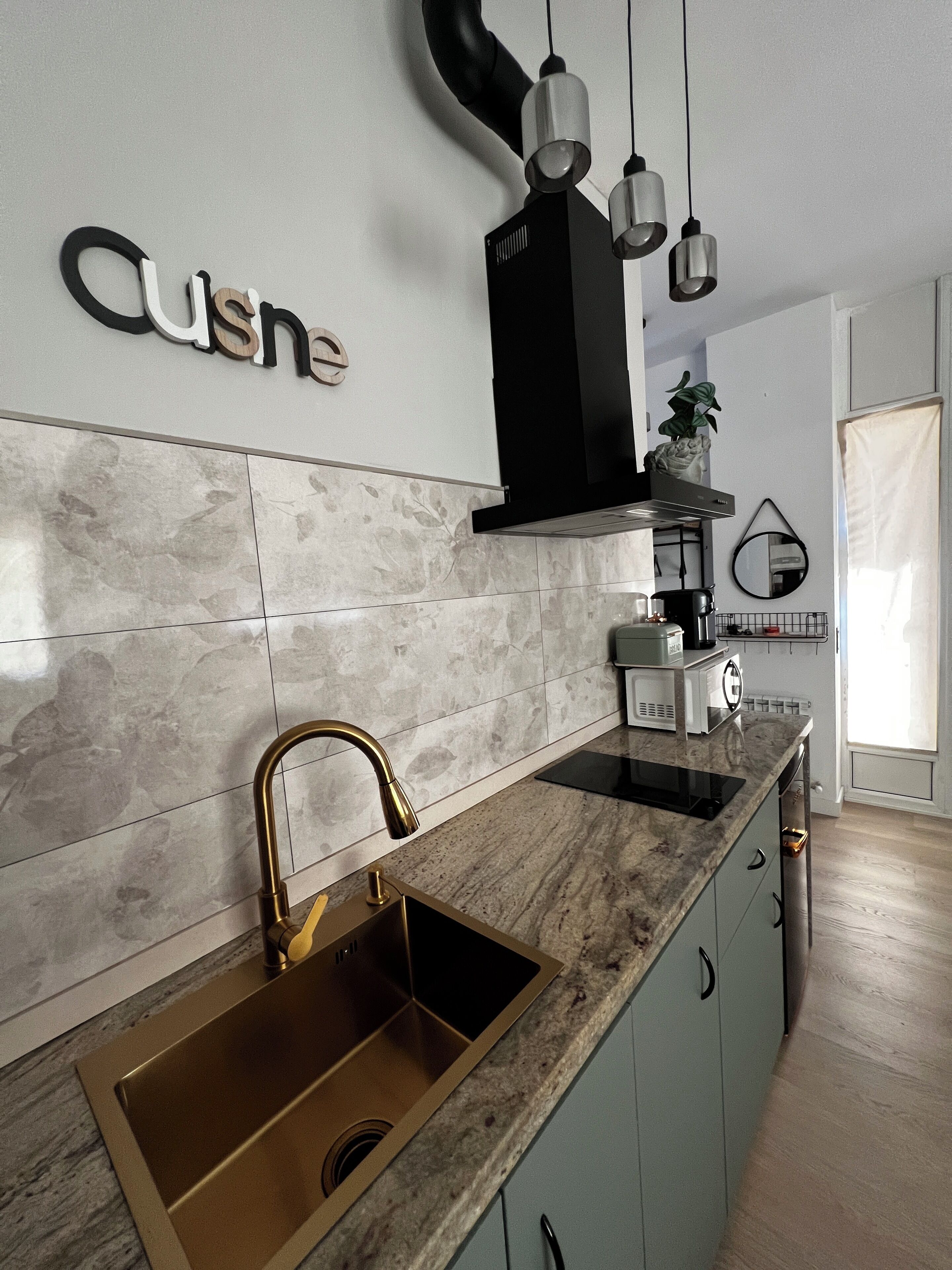 Una cocina moderna con encimera de mármol, grifo dorado y campana extractora negra.