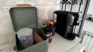 Et tekøkken med kaffemaskine, et brødskrin og diverse køkkenredskaber.