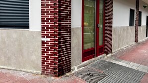 A building facade with a red door, a window with a closed shutter, and a metal grate at the entrance. - La Arquita, tu apartamento en Valladolid (Valladolid)