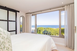 Une chambre avec un grand lit, une vue sur la mer et une fenêtre avec des rideaux.