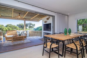 An outdoor dining area with a wooden table and chairs, a wicker sofa, and a grill. - Pikkewyntjie | Sea view | Small families (Vermont)