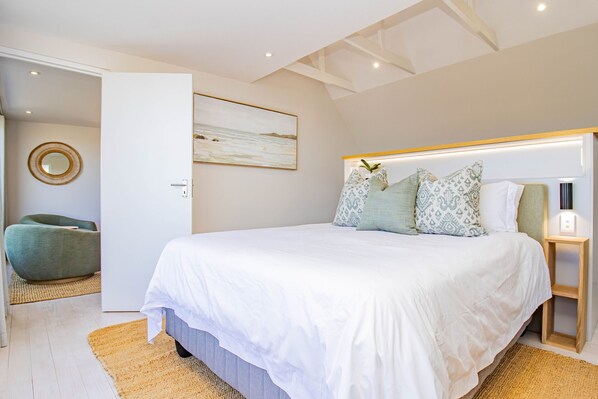 Une chambre avec un grand lit, une table de chevet avec une lampe, un miroir fixé au mur et un fauteuil vert.