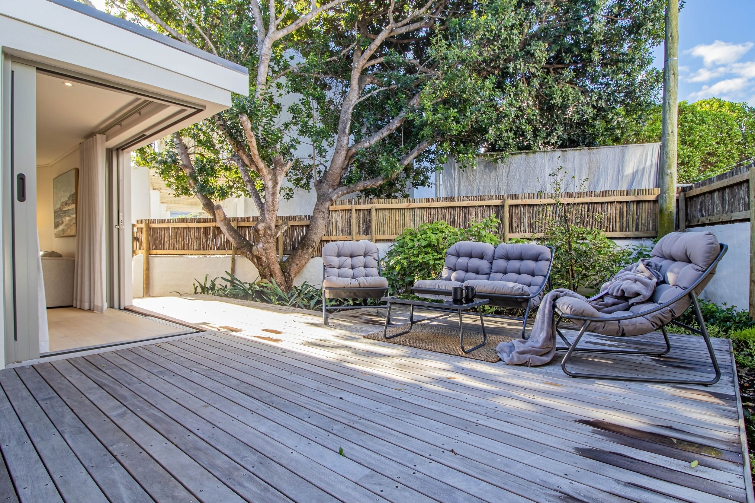 Une terrasse extérieure avec un plancher en bois, des chaises rembourrées et une petite table.