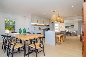 A modern kitchen with white cabinets, a wooden dining table, and a central island with stools. - Pikkewyntjie | Sea view | Small families (Vermont)