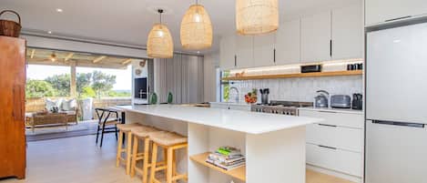 Una cocina moderna con una isla central, luces colgantes y vistas al exterior.