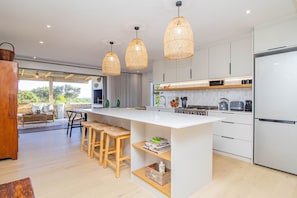 Une cuisine moderne dotée d’un îlot central, de luminaires suspendus et offrant une vue sur l’extérieur.