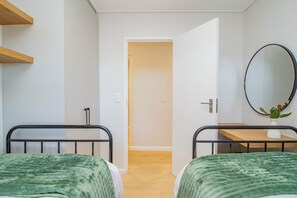 A room with two beds, a wooden shelf, a mirror, and a door leading to another room.