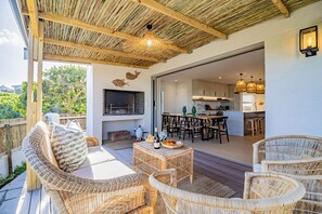An outdoor patio with wicker furniture, a grill, and a dining area with a kitchen in the background.