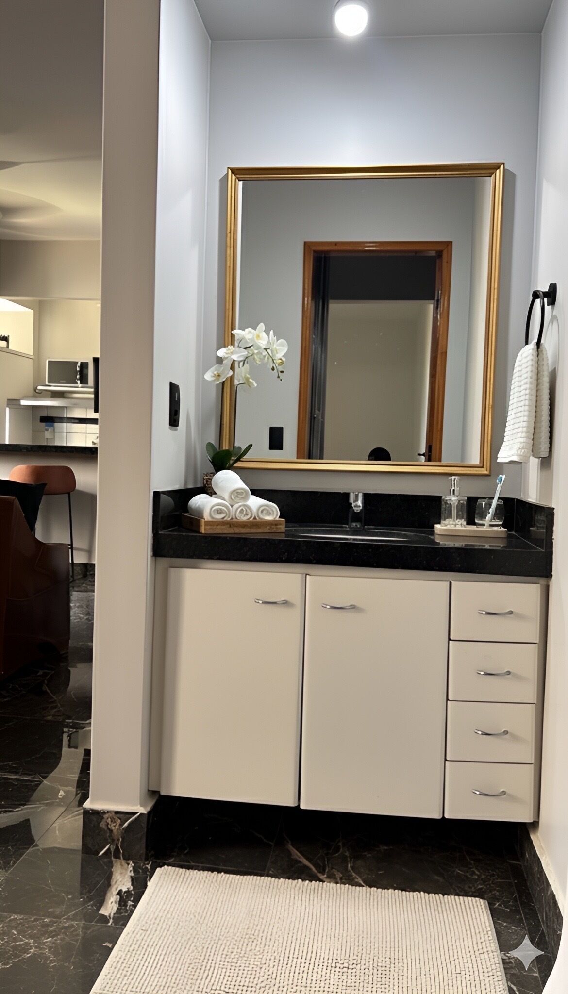 A modern bathroom with a large mirror, white cabinets, a black countertop, and a small potted orchid.