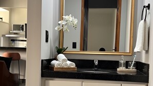 Un baño moderno con un espejo grande, muebles blancos, encimera negra y una pequeña orquídea en maceta.