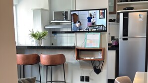Una cocina moderna con televisión, taburetes de bar, suelo de mármol y una mesa de comedor.