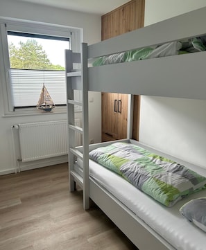 A bunk bed room with a window, radiator, and a small sailboat decoration.