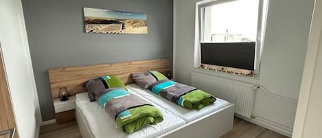 Une chambre moderne avec une tête de lit en bois, une grande fenêtre et un tableau sur le thème de la plage accroché au mur.
