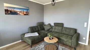 Ein modernes Wohnzimmer mit einem Ecksofa, einem runden Couchtisch aus Holz und einem Gemälde mit Strandmotiv.