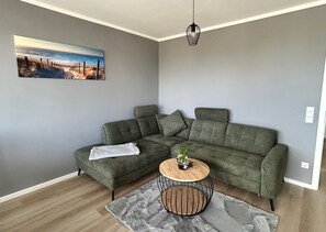 A modern living room with a sectional sofa, a round wooden coffee table, and a painting of a beach scene.