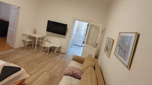 A living room with a sofa, a TV, a dining table, and chairs. There is a door leading to another room. - Modern 2BR Apt Near Karlsplatz (Vienna)