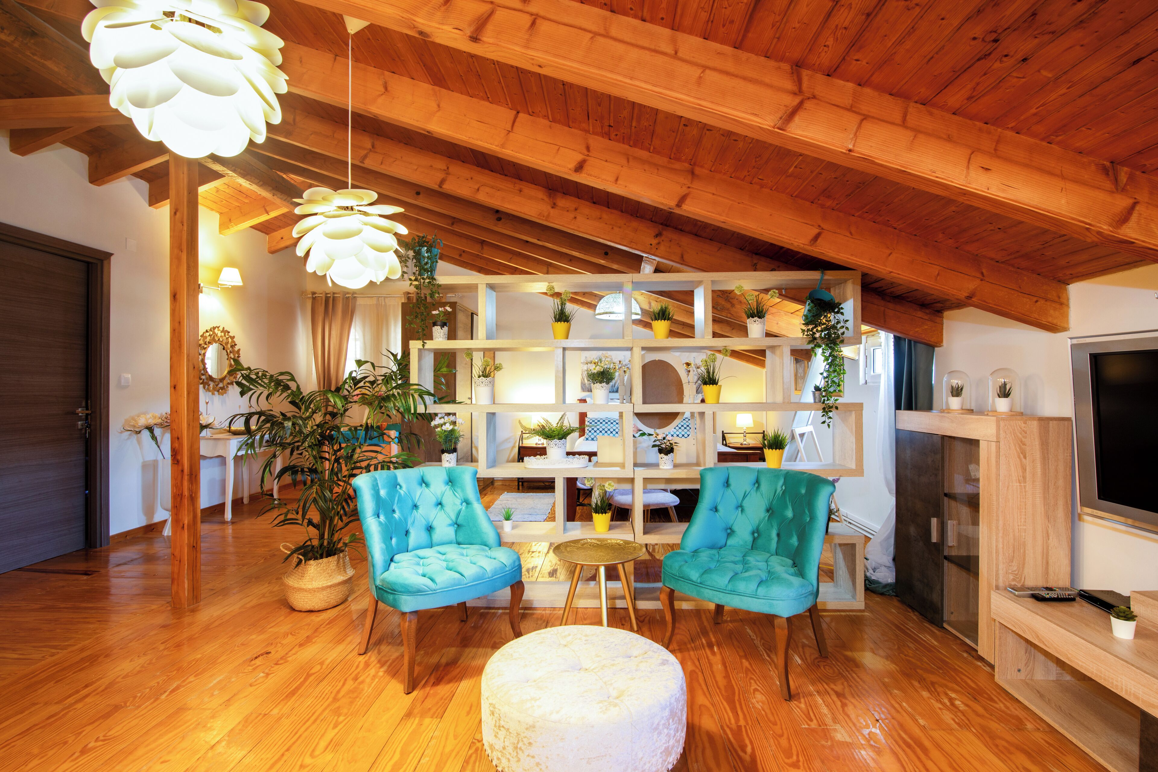 A cozy living room with wooden flooring, two teal armchairs, a white ottoman, and a wooden TV stand.