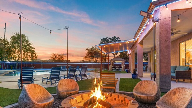 A fire pit with seating, a pool, and a covered patio area.