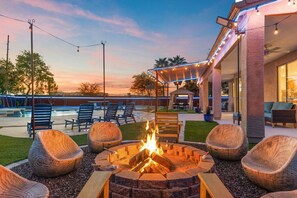 A fire pit with seating, a pool, and a covered patio area.
