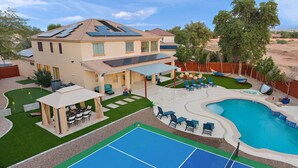 A house with a swimming pool, a tennis court, and a covered patio area.