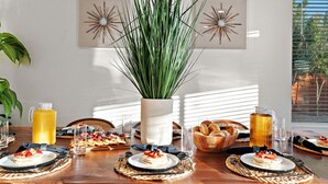 A breakfast table with plates of food, a pitcher of orange juice, and a large plant in the center.