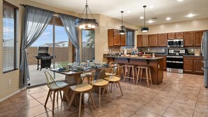A spacious kitchen with a central island, bar stools, and a dining table set for a meal. - Chill & Thrill | Pool, Hot Tub • Family Game Villa (Casa Grande)