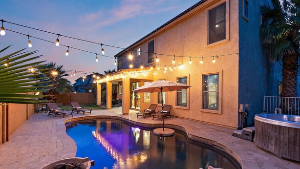 A swimming pool with lounge chairs and a hot tub, surrounded by a patio area with string lights. - Chill & Thrill | Pool, Hot Tub • Family Game Villa (Casa Grande)