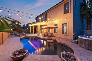 A swimming pool with lounge chairs and a hot tub, surrounded by a patio area with string lights.