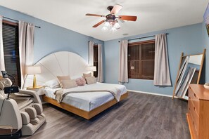 A bedroom with a bed, a ceiling fan, a desk, and a chair.