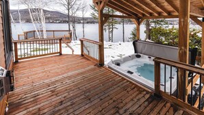 Une terrasse en bois avec un jacuzzi, une pergola en bois et une vue sur un lac et des montagnes.