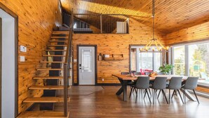 Un intérieur en bois avec un escalier, un coin repas et de grandes fenêtres.