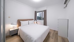 Moderni hotellihuone, jossa on suuri sänky, yöpöydällä olevat lamput, vaatekaappi ja ikkuna, jossa on verhot.