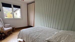 A bedroom with a bed, a chair, a window with curtains, and a wooden floor. - Gd appartement cozy 85 M2 2chb + grande mezzanine accès funiculaire les arcs (Bourg-Saint-Maurice)