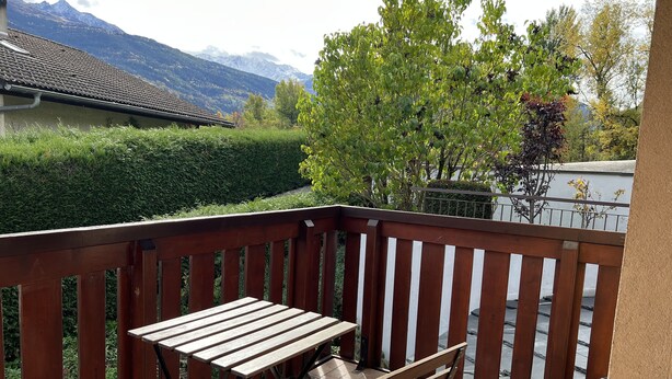 A wooden deck with a table and chairs, overlooking a mountainous landscape and a neatly trimmed hedge. - Gd appartement cozy 85 M2 2chb + grande mezzanine accès funiculaire les arcs (Bourg-Saint-Maurice)
