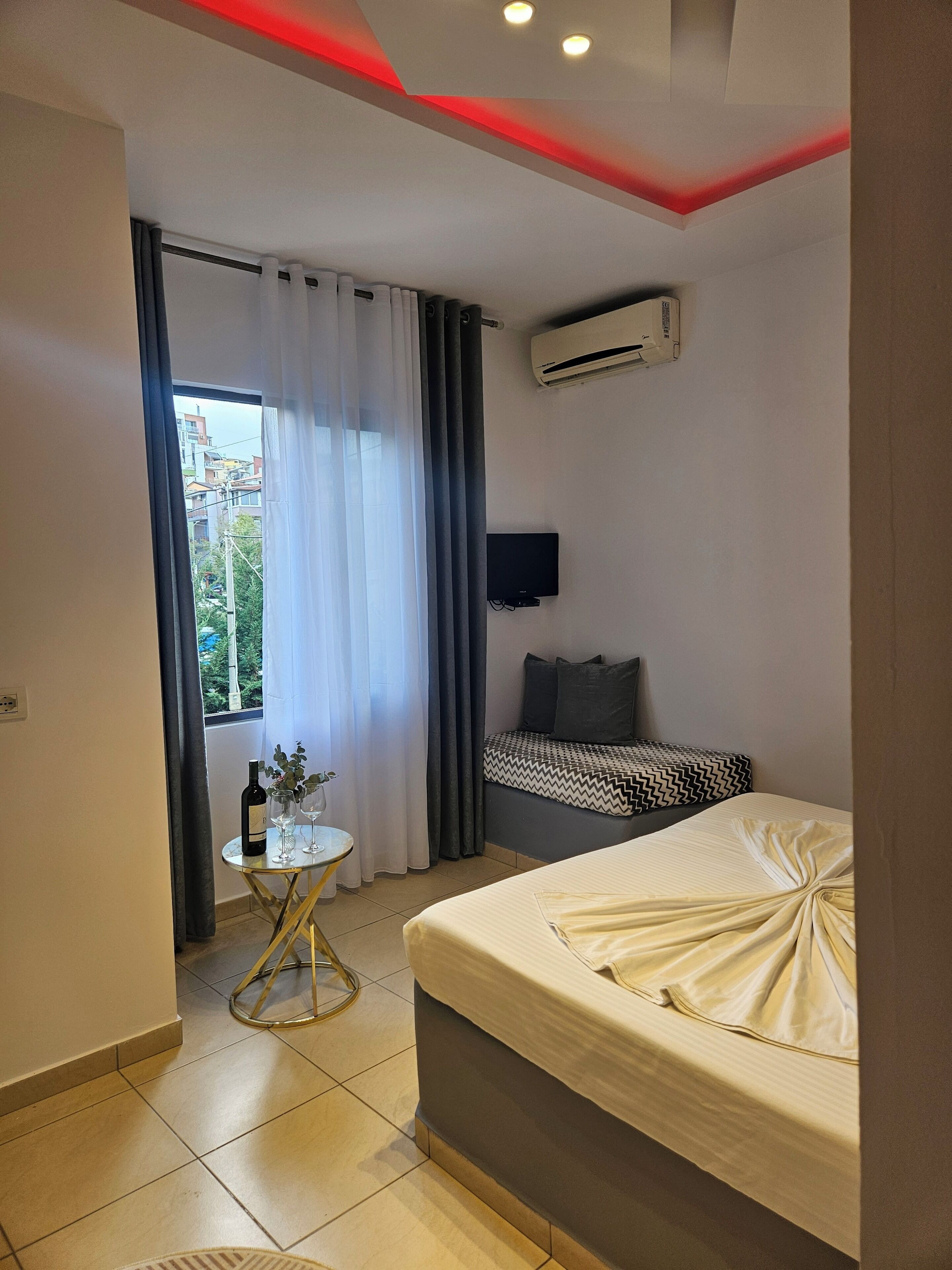 A modern bedroom with a bed, a small table with wine glasses, and a TV on the wall.