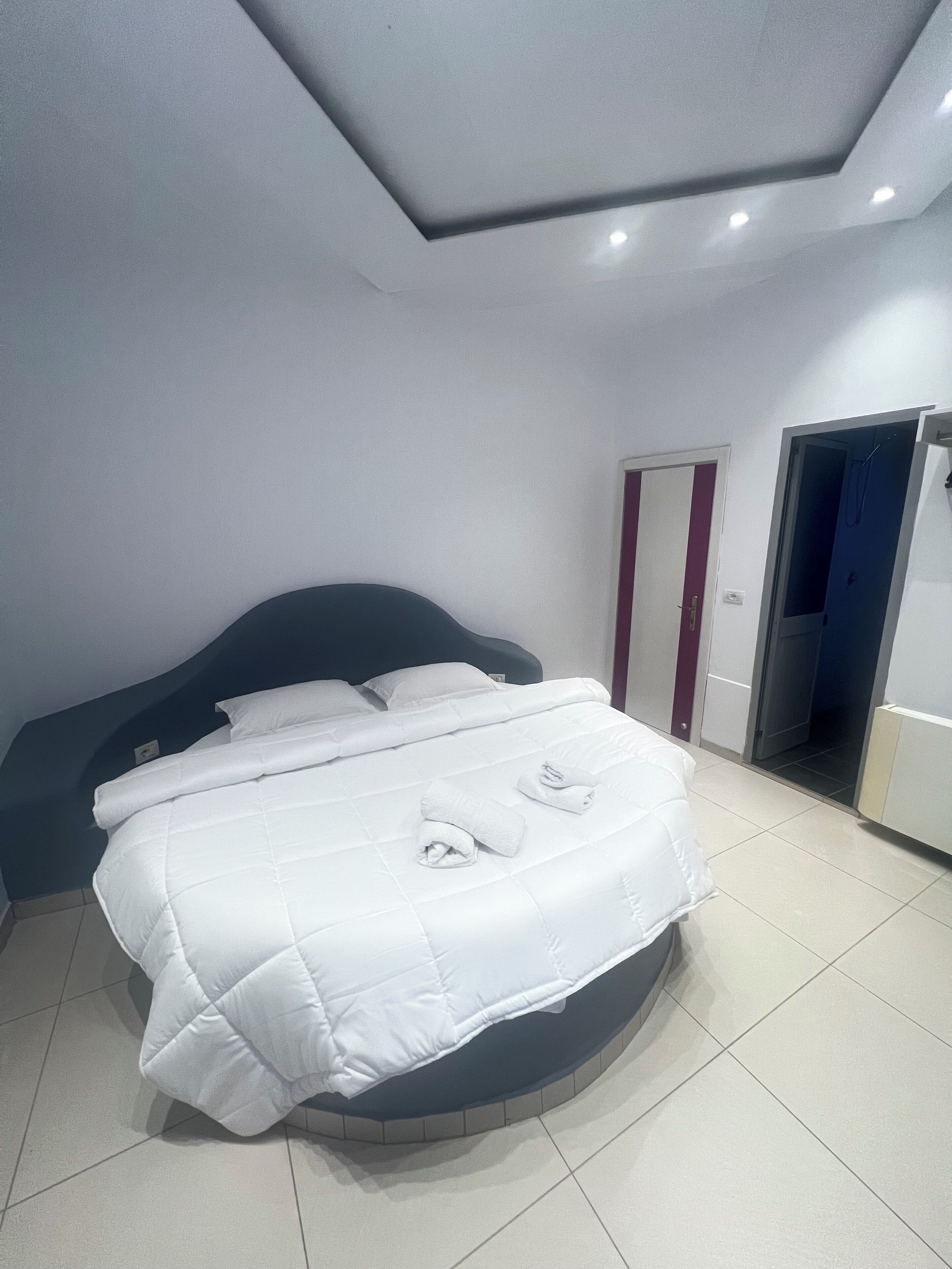 Ein modernes Schlafzimmer mit einem gebogenen Bett, weißer Bettwäsche und einer Tür zu einem Badezimmer.