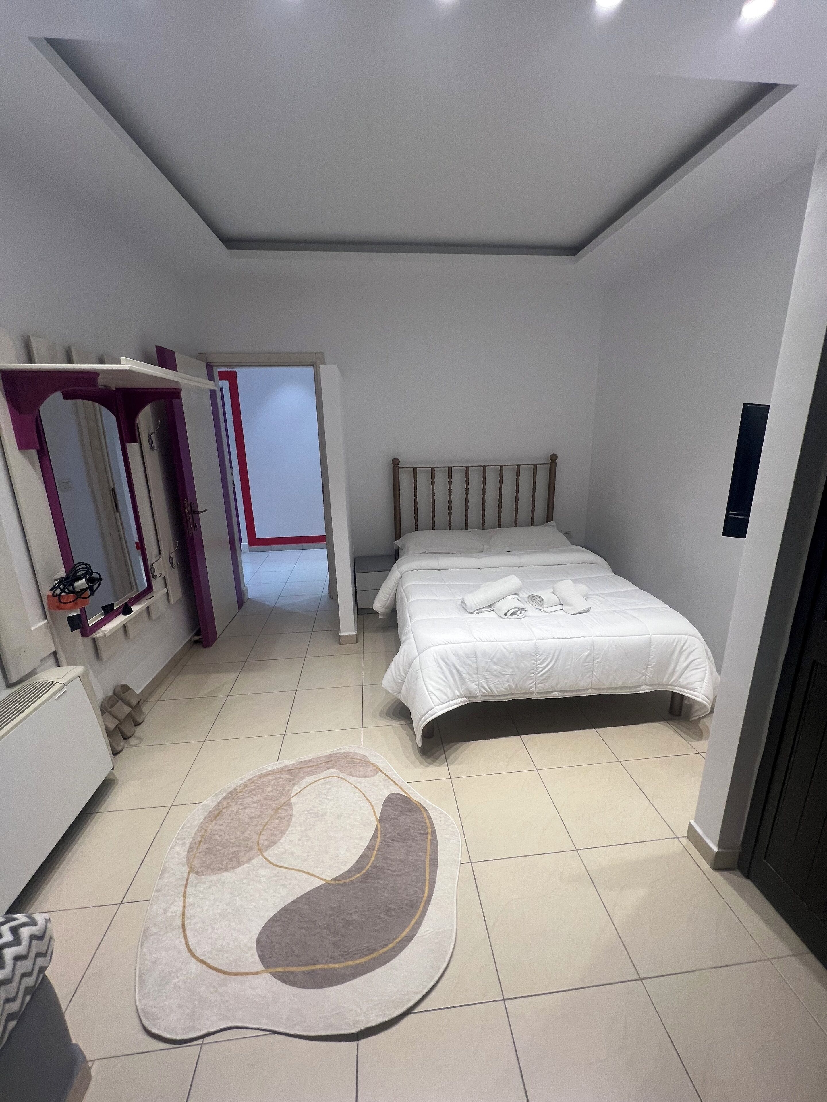 Quarto com cama, espelho, guarda-roupa e porta que dá para outro cômodo.