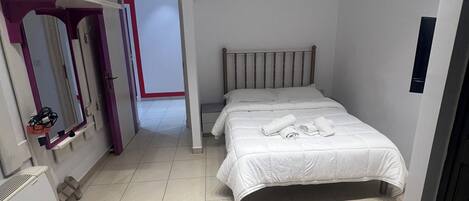 Quarto com cama, espelho, guarda-roupa e porta que dá para outro cômodo.