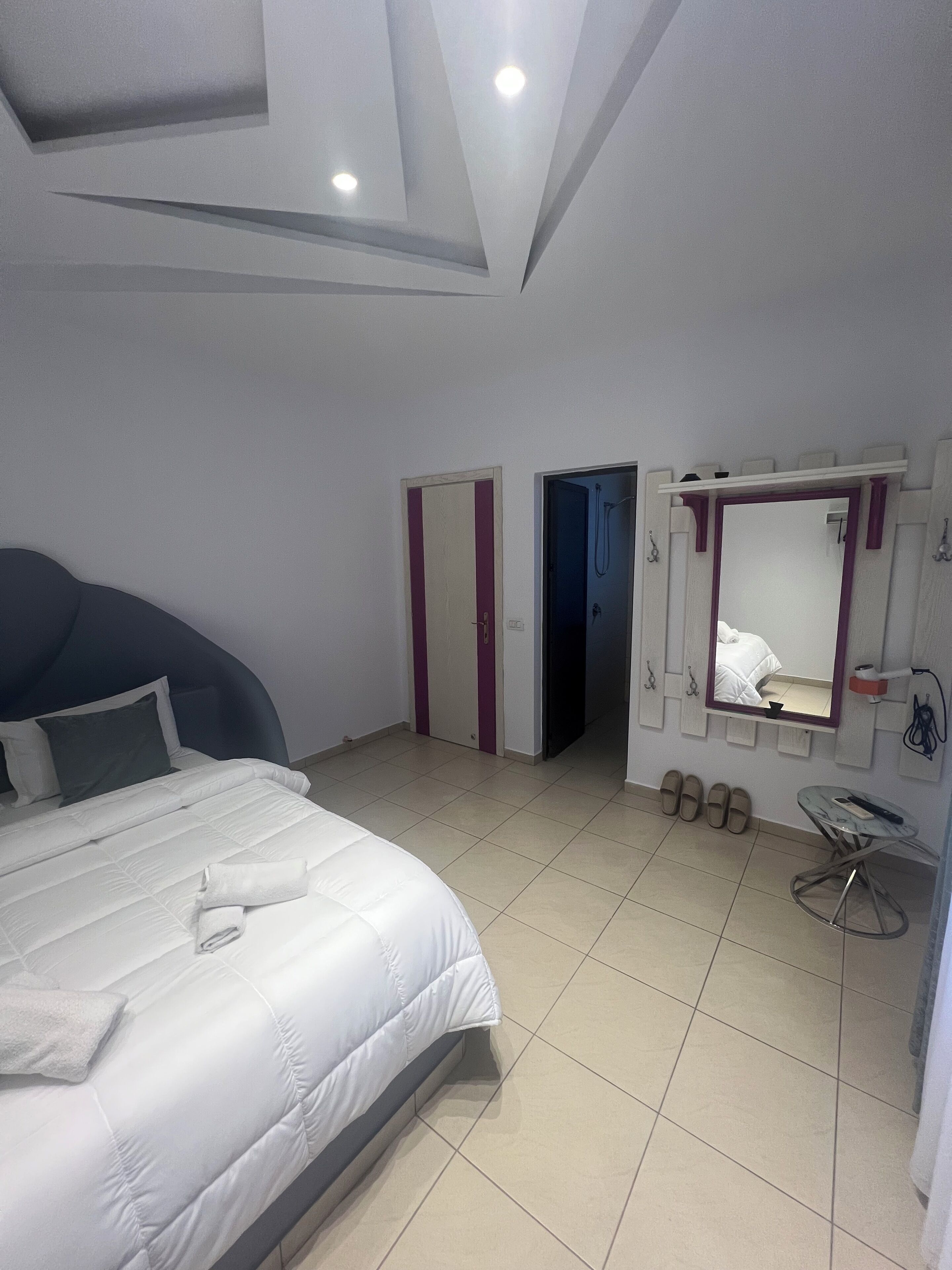 A modern hotel room with a bed, a bathroom with a mirror, and a small table.
