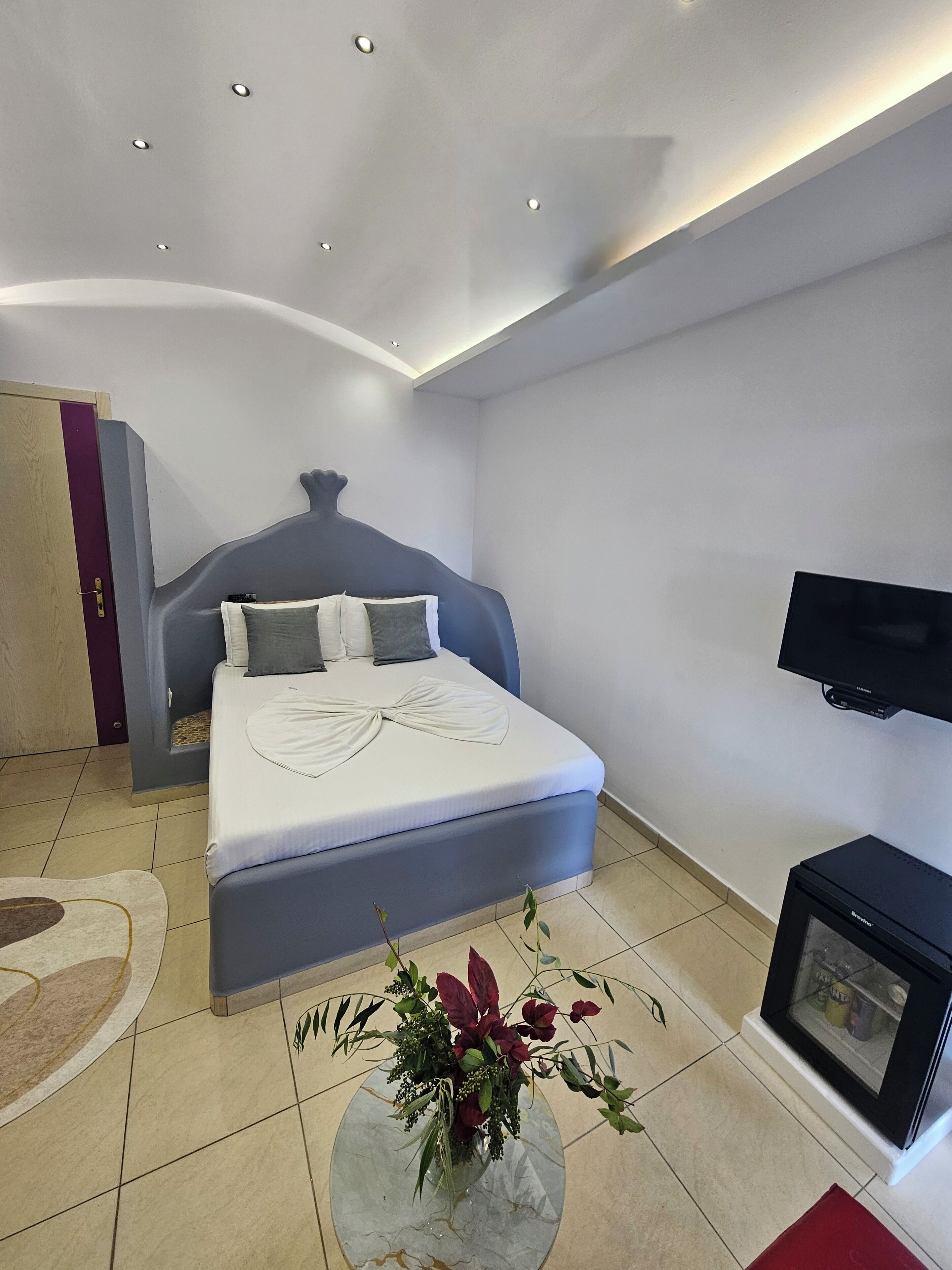 Un dormitorio moderno con una cama, un televisor de pantalla plana, un televisor pequeño y un jarrón decorativo.