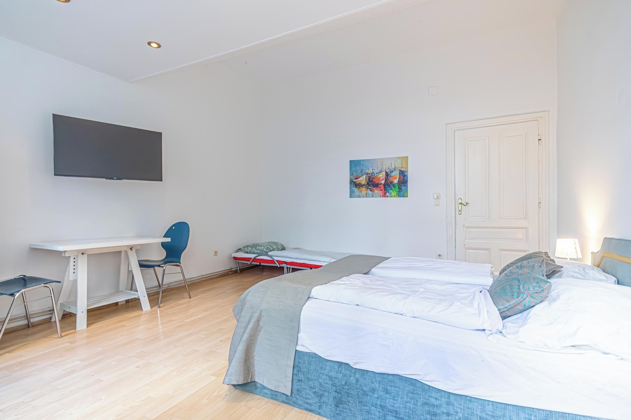 Een slaapkamer met een bed, een bureau, een stoel, een televisie en een deur.