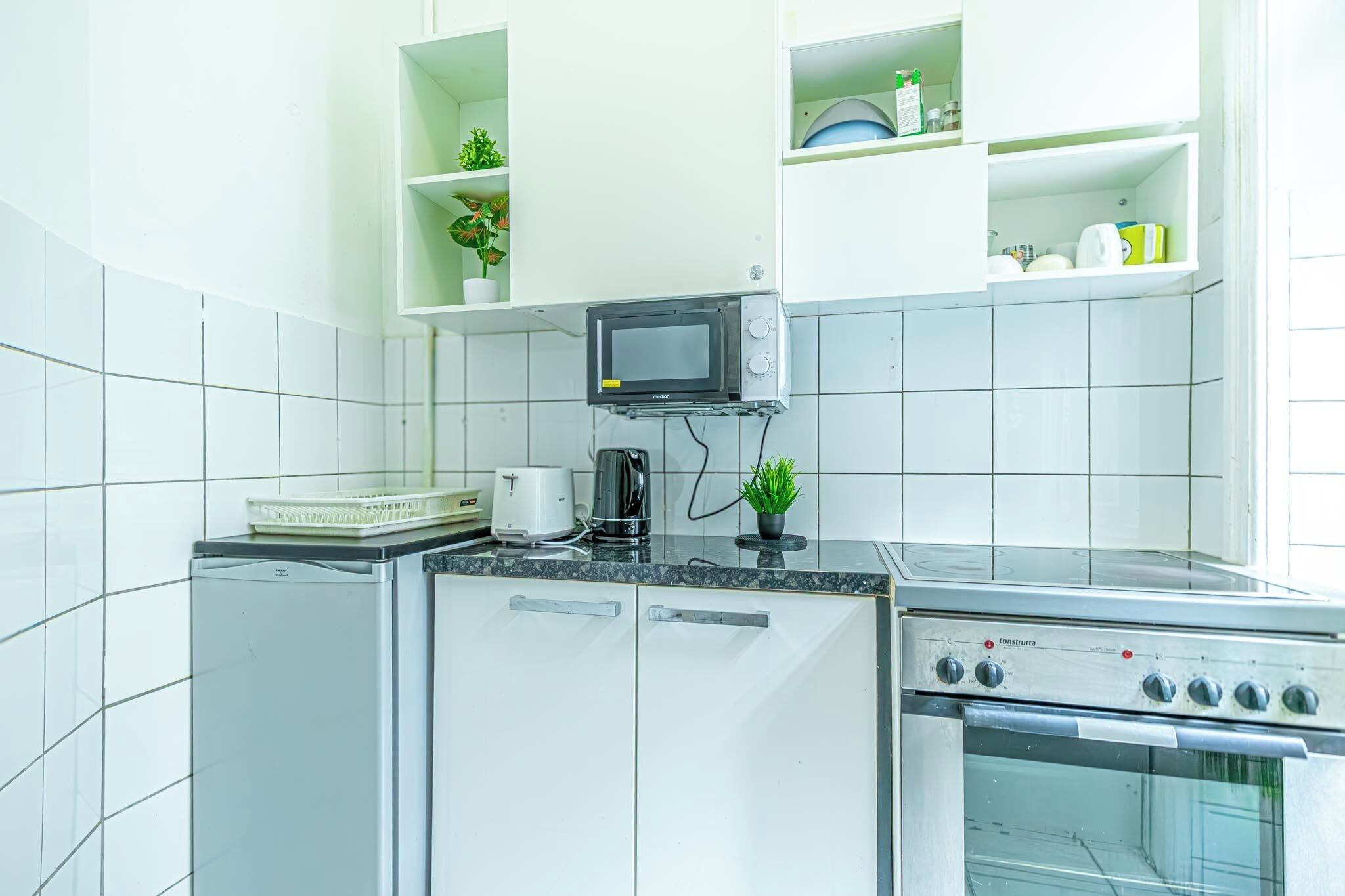 Uma cozinha compacta com armários brancos, micro-ondas, cafeteira e forno embutido.