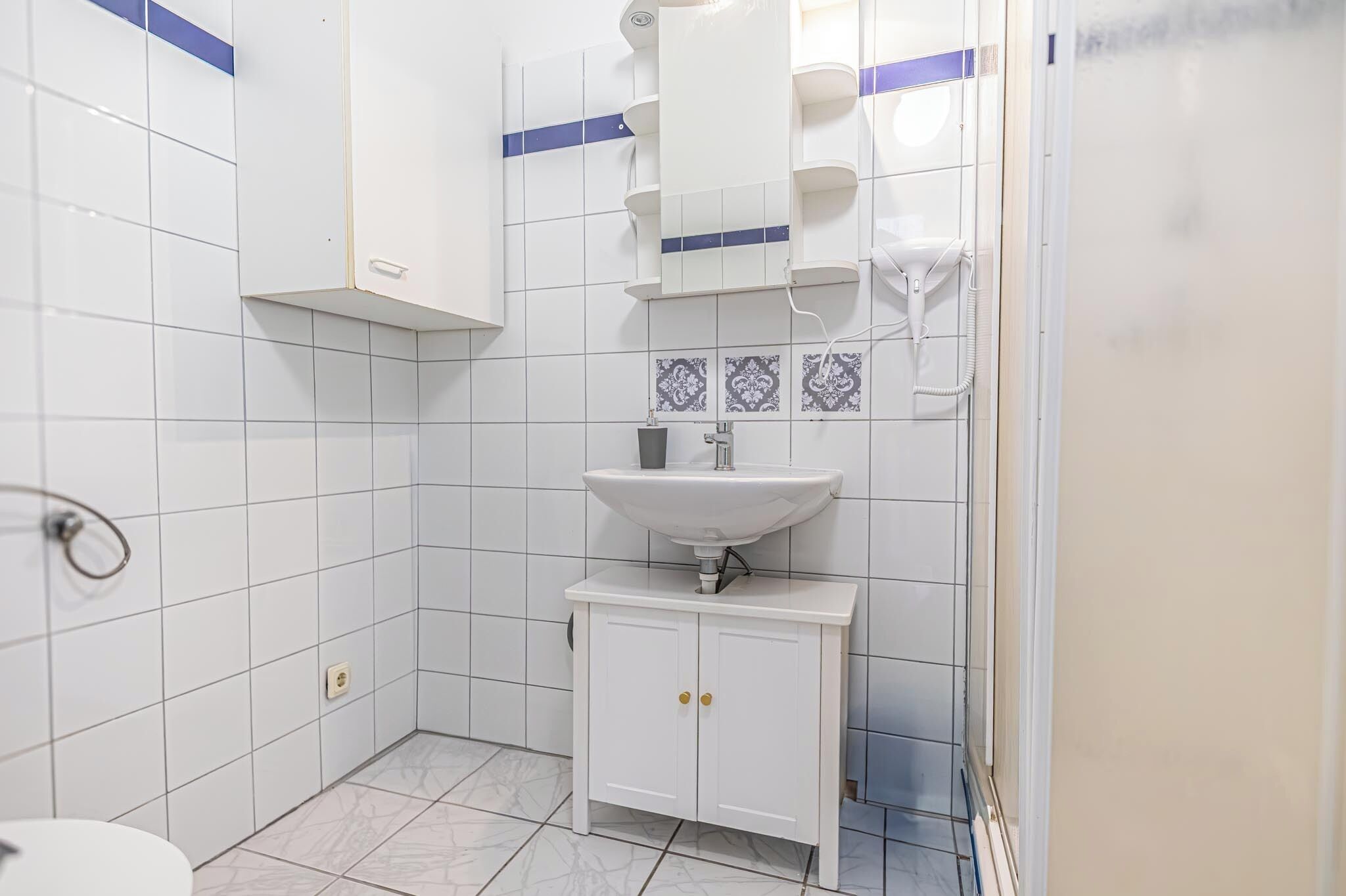 Une salle de bain avec des carreaux blancs, un lavabo, un miroir et un porte-serviettes.