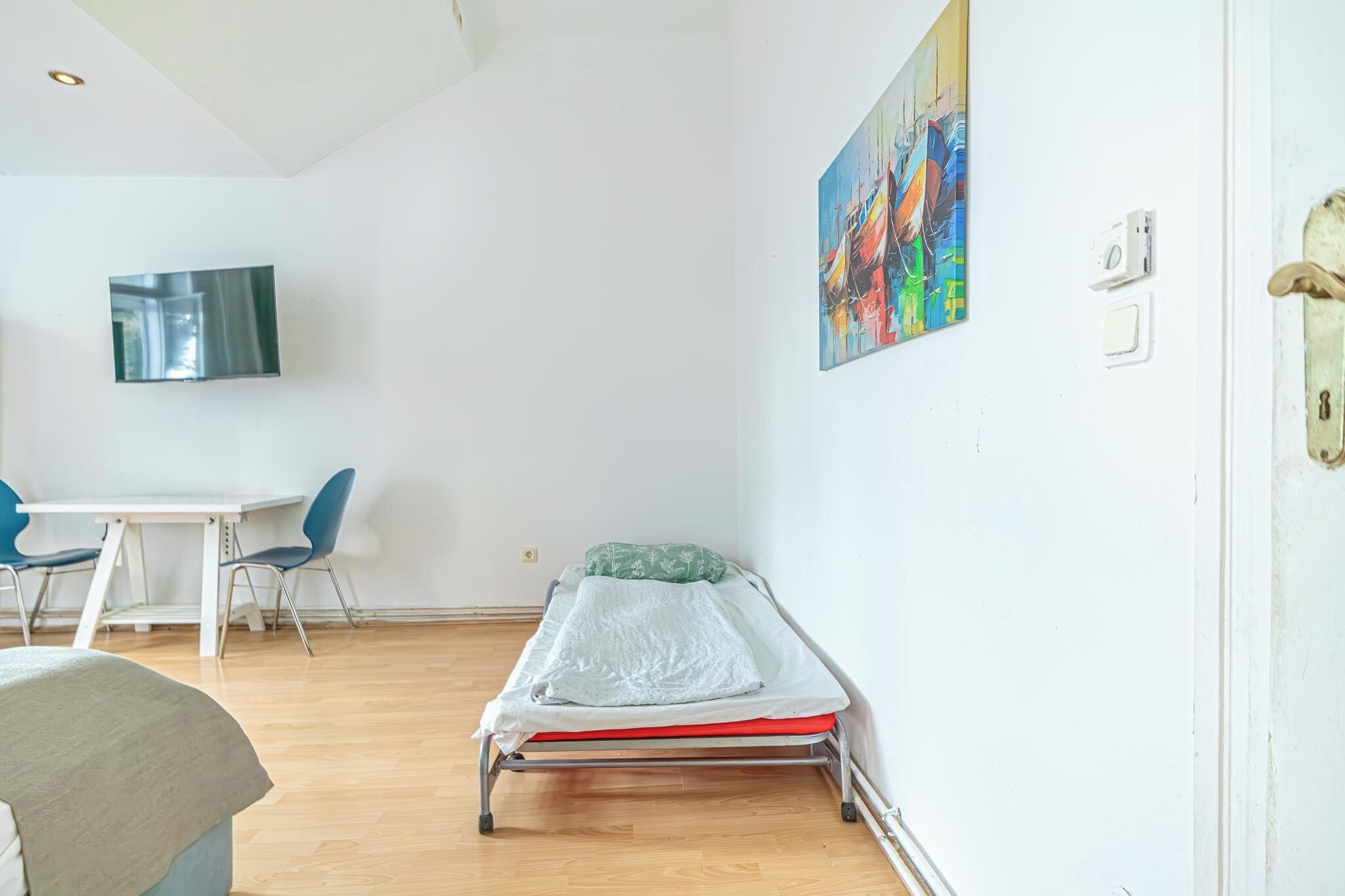 A small, bright room with a bed, a table, and chairs.
