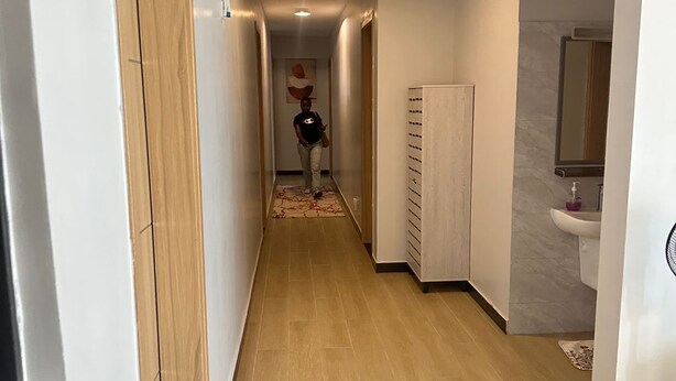 A hallway with wooden flooring, white walls, and a tiled floor leading to a bathroom with a sink and mirror. - Spacious 5-bedroom apartment in terrific Nairobi -White Oak Residency with AC, (Nairobi)