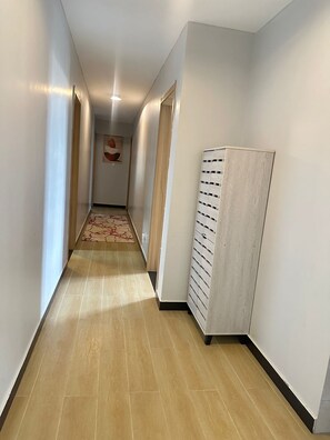 Un couloir doté d’un plancher en bois, de murs blancs et d’une armoire de couleur claire adossée au mur.
