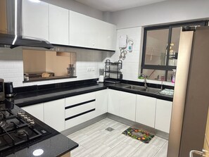 Una cucina moderna con mobili bianchi, piani di lavoro neri, una cappa aspirante in acciaio inossidabile, un forno integrato e una finestra con vista.
