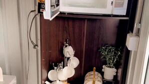 A compact kitchen with a microwave, shelves with dishes, and a variety of condiments. - “Private Bedroom & Large Deck + Separate Entrance” (Papatoetoe)