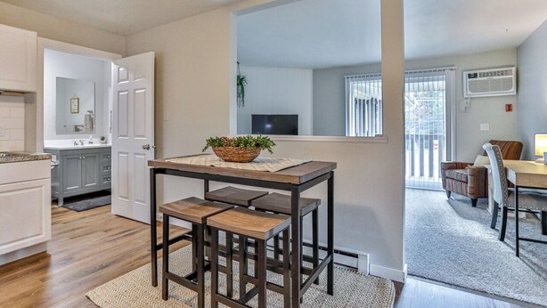 Une cuisine moderne avec des meubles blancs, un plan de travail en bois et un coin repas comprenant une table et des bancs.