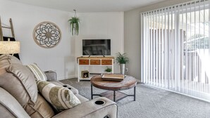 Un salon avec un canapé, une table basse, un téléviseur et une porte-fenêtre coulissante.